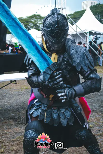 A cosplayer in dark knight armor holding a blue sword